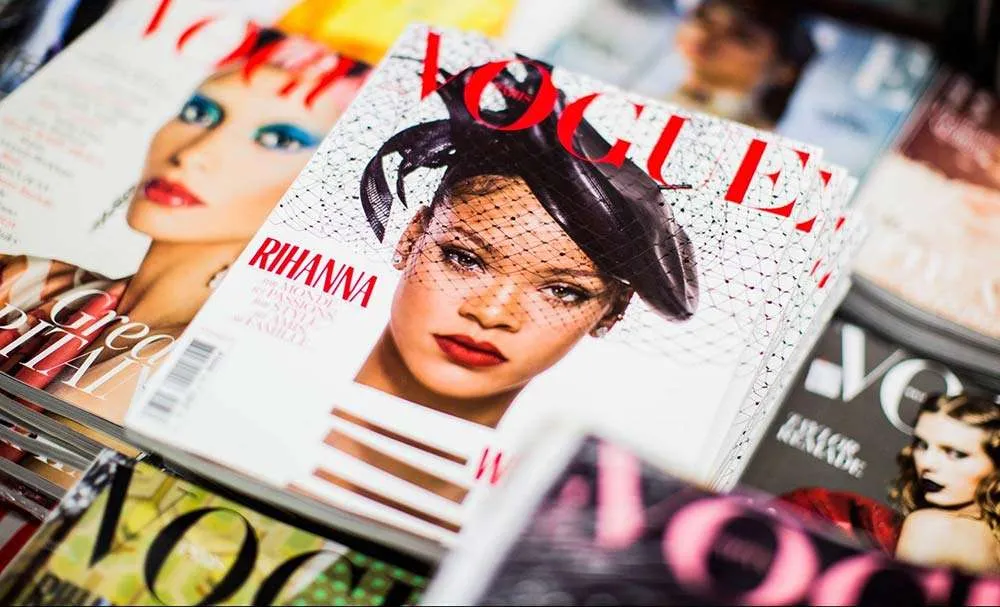 Table with many magazines including Vogue magazine cover with Rihanna on it's Cover