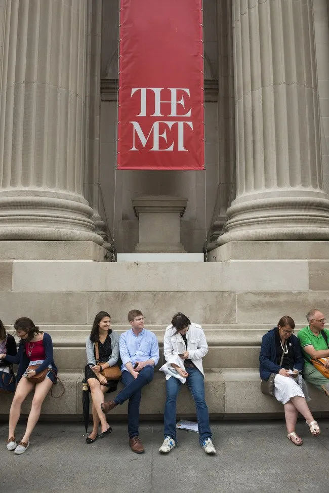 People sitting in front of the met with a red print banner hanging overhead